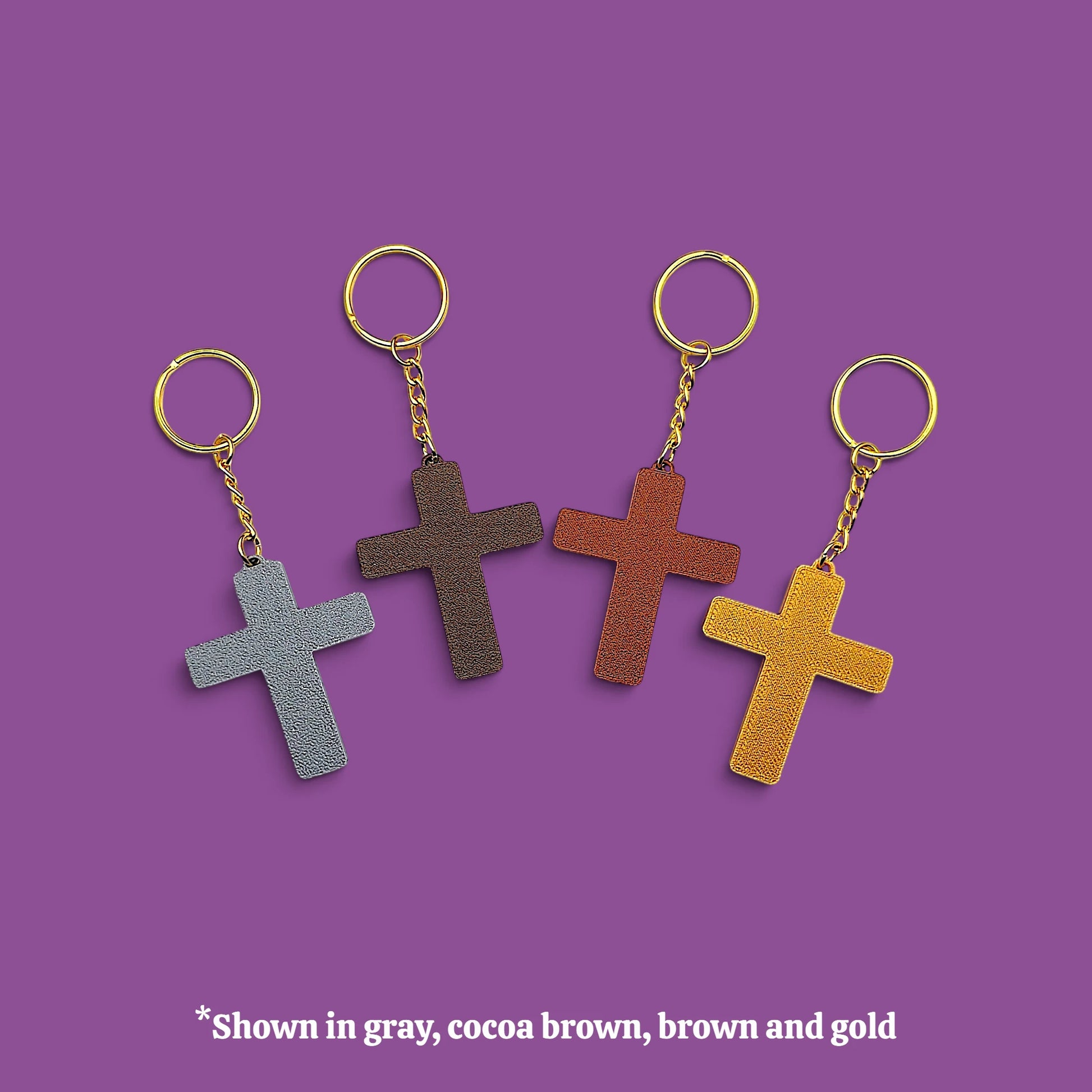 Four textured cross keychains in gray, cocoa brown, brown, and mustard yellow, each with gold-tone rings and chains, displayed on a solid purple background with a text overlay at the bottom.