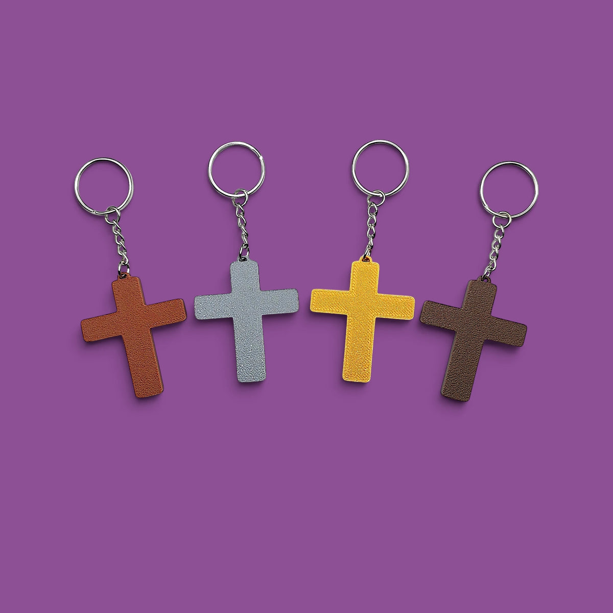 Four cross-shaped keychains in different colors in a row on a solid purple background.