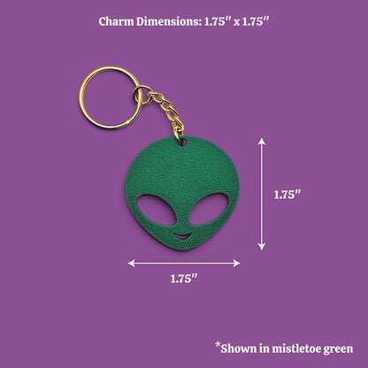 A green alien-head keychain with a gold key ring and chain, shown on a purple background with dimension labels indicating 1.75 inches by 1.75