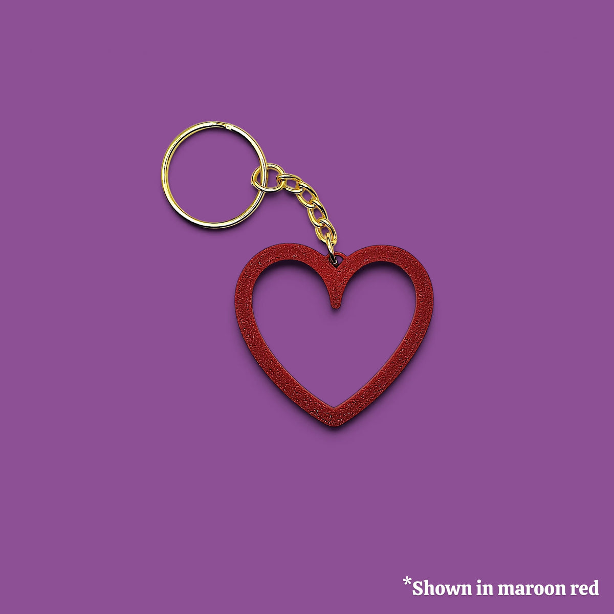 A heart-shaped keychain with a maroon red textured outline and a gold-tone metal split ring and chain, shown on a solid purple background with a small text note in the bottom right corner.
