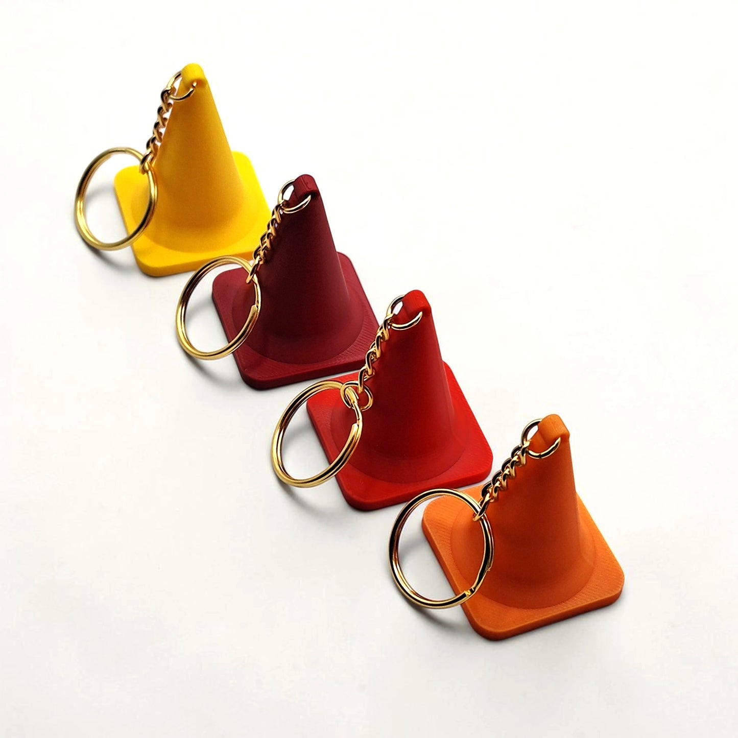 Four traffic cone keychains in yellow, red, and orange on a white background