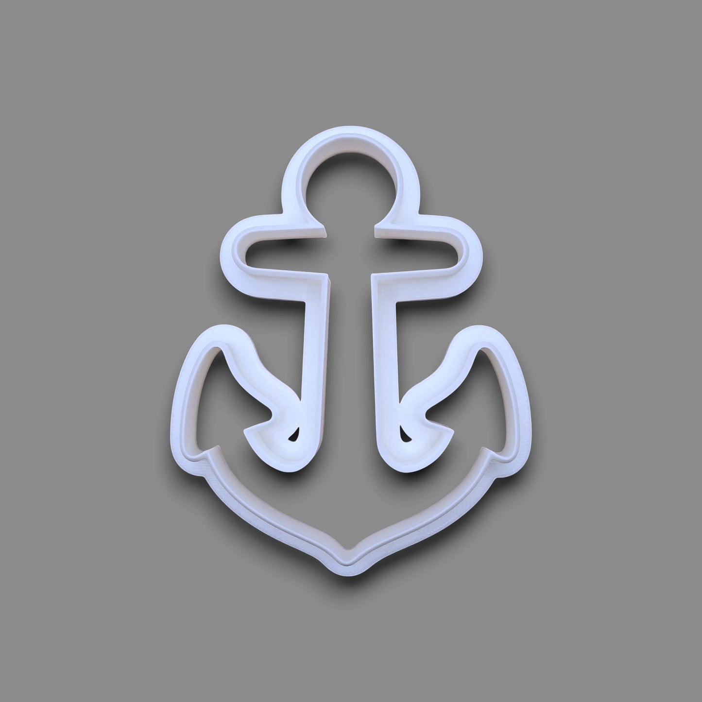 A white plastic anchor-shaped cookie cutter, shown from a top-down view on a solid gray background.