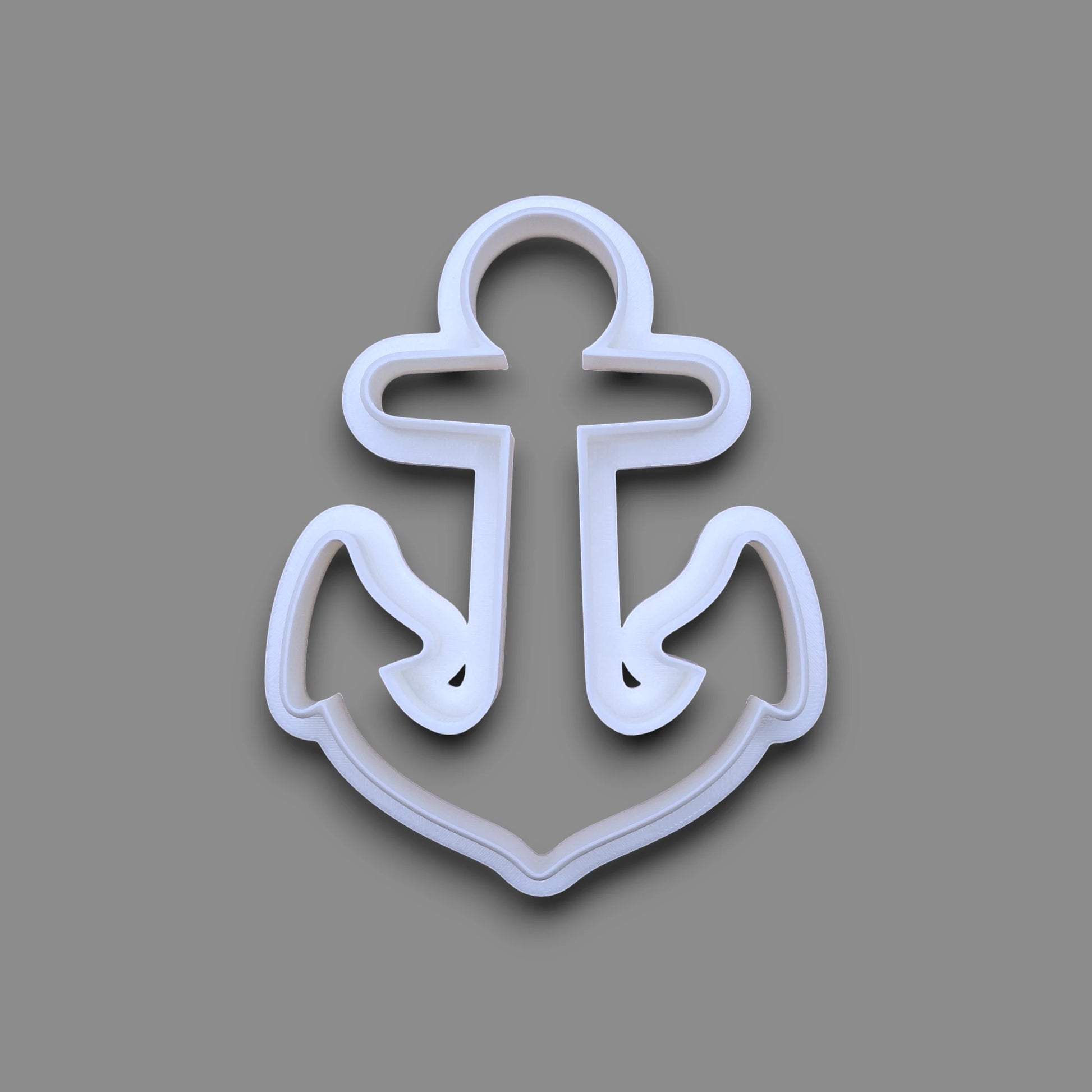A white plastic anchor-shaped cookie cutter, shown from a top-down view on a solid gray background.