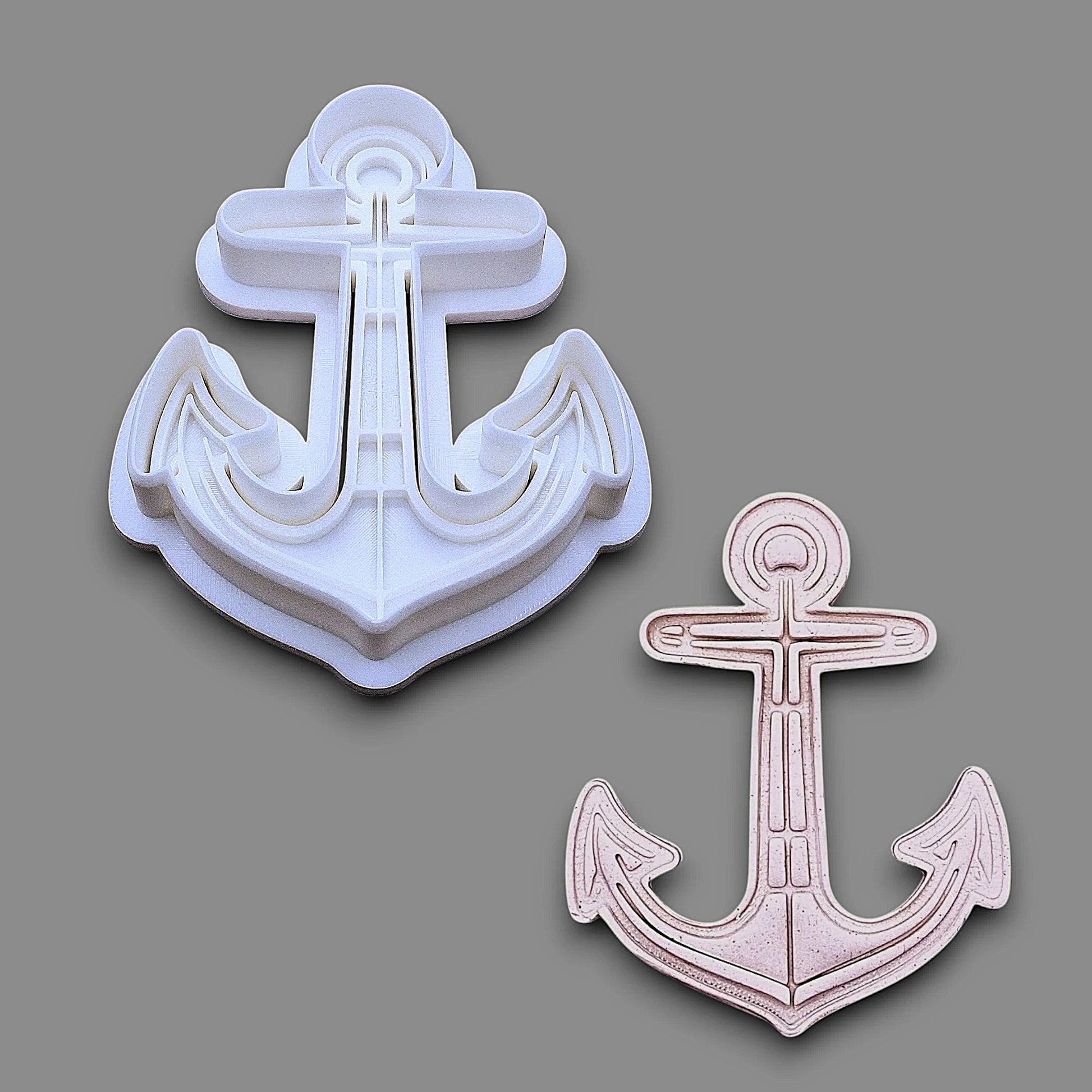 A white plastic anchor-shaped baking and craft cookie cutter shown on a gray background, alongside a smaller matching anchor-shaped dough cutout and imprint.