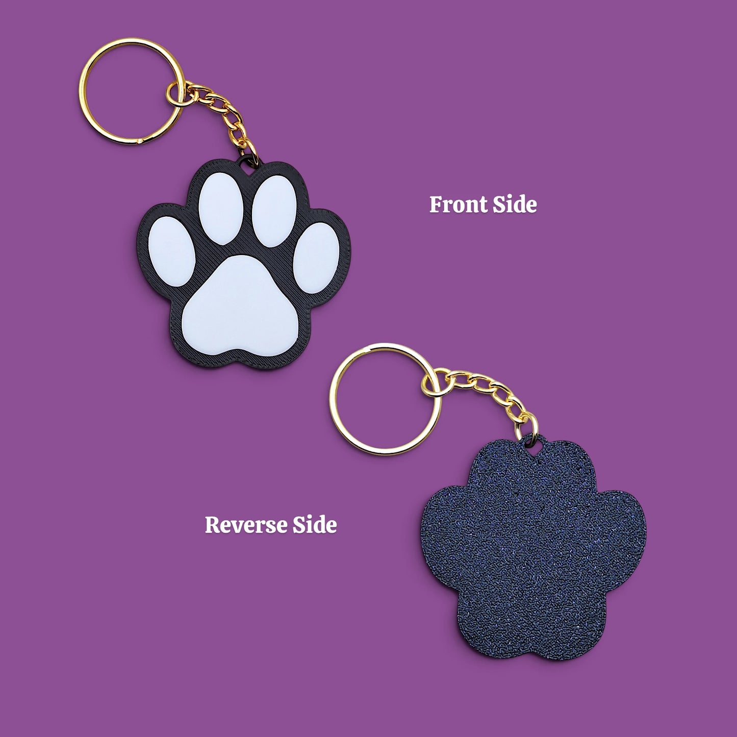 Two paw-shaped keychains shown on a purple background, labeled 'Front Side' and 'Reverse Side.' The top keychain shows a black paw pad with pale blue-gray pads and a gold key ring and chain.