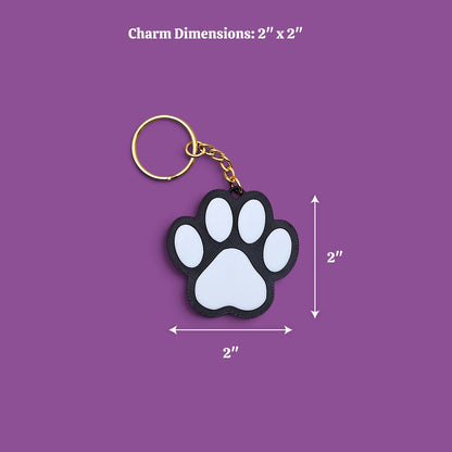 A paw-shaped keychain with a black and white design and a gold key ring, shown on a purple background with dimension labels indicating 2 x 2 inches.