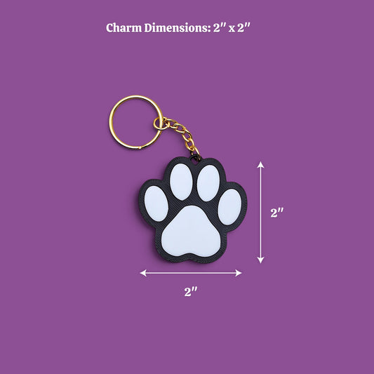 A paw-shaped keychain with a black and white design and a gold key ring, shown on a purple background with dimension labels indicating 2 x 2 inches.
