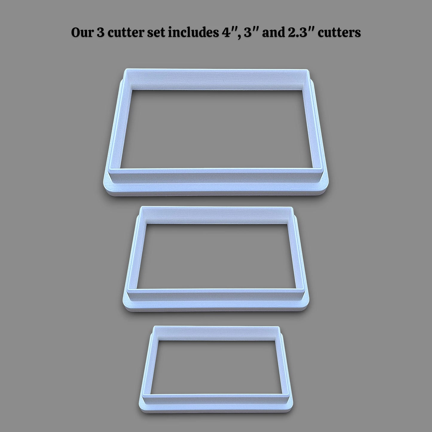 Three rectangular cookie cutters in sizes 4 inches, 3 inches, and 2.3 inches, displayed vertically on a solid gray background with black text at the top stating 'Our 3 cutter set includes 4", 3" and 2.3" cutters'