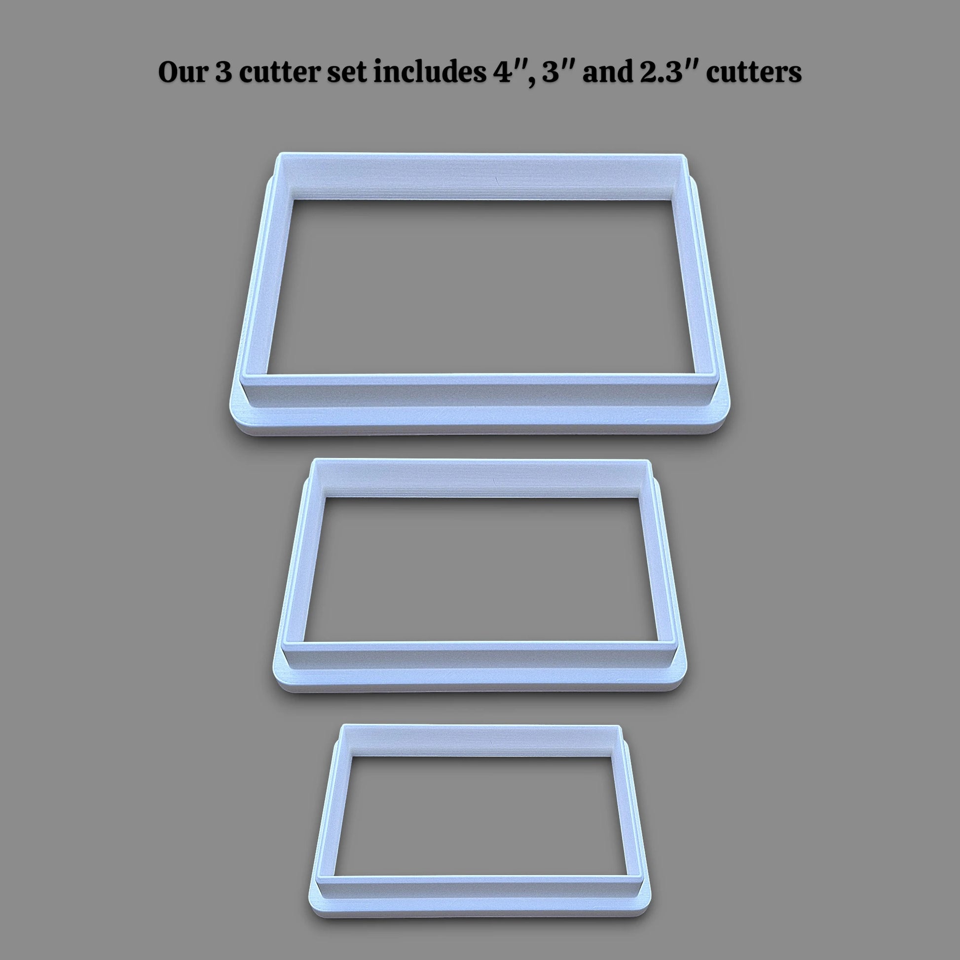 Three rectangular cookie cutters in sizes 4 inches, 3 inches, and 2.3 inches, displayed vertically on a solid gray background with black text at the top stating 'Our 3 cutter set includes 4", 3" and 2.3" cutters'