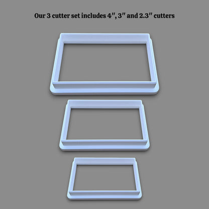Three rectangular cookie cutters in sizes 4 inches, 3 inches, and 2.3 inches, displayed vertically on a solid gray background with black text at the top stating 'Our 3 cutter set includes 4", 3" and 2.3" cutters'