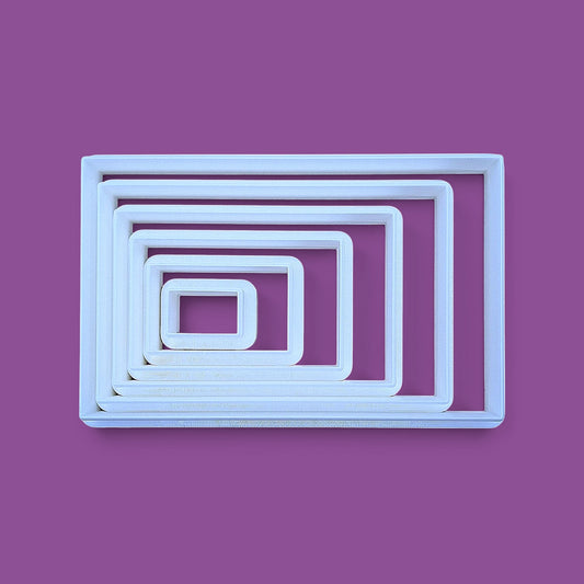 A rectangular cookie cutter set, photographed from above on a purple background.