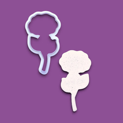 A rose cookie cutter and matching dough cutout shown on a solid purple background.