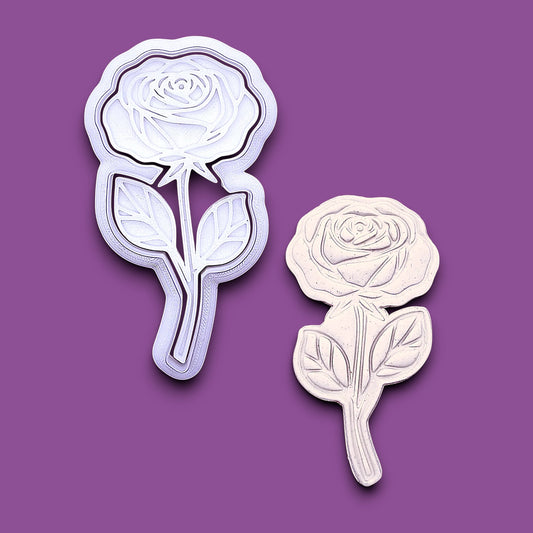 A white rose-shaped cookie cutter and matching rose-shaped clay mold shown on a solid purple background.