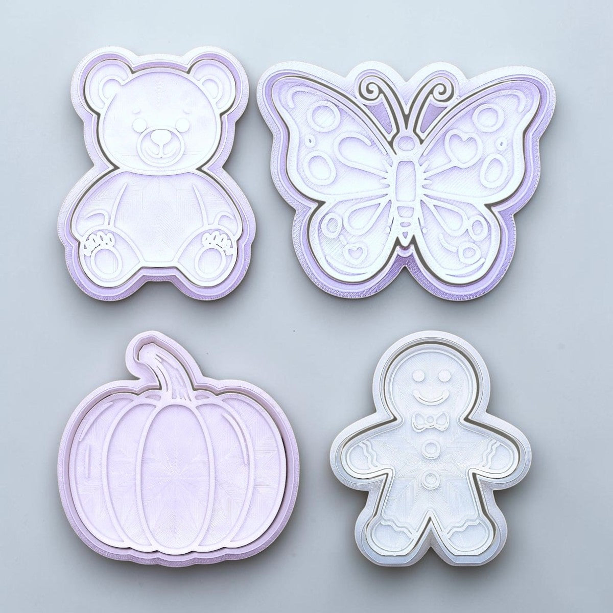 Set of four cookie cutters shaped like a teddy bear, butterfly, pumpkin, and gingerbread man on a light gray background.