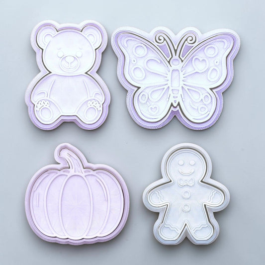 Set of four cookie cutters shaped like a teddy bear, butterfly, pumpkin, and gingerbread man on a light gray background.