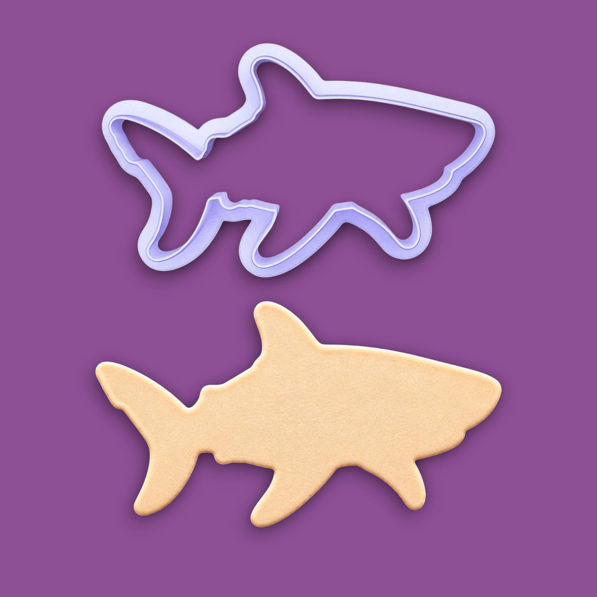 A plastic shark-shaped cookie cutter shown above a cookie cutout of the same shape, set against a solid purple background.
