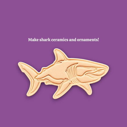 A shark-shaped ceramic or clay mold and template shown on a solid purple background, with the text 'Make shark ceramics and ornaments!' above it.