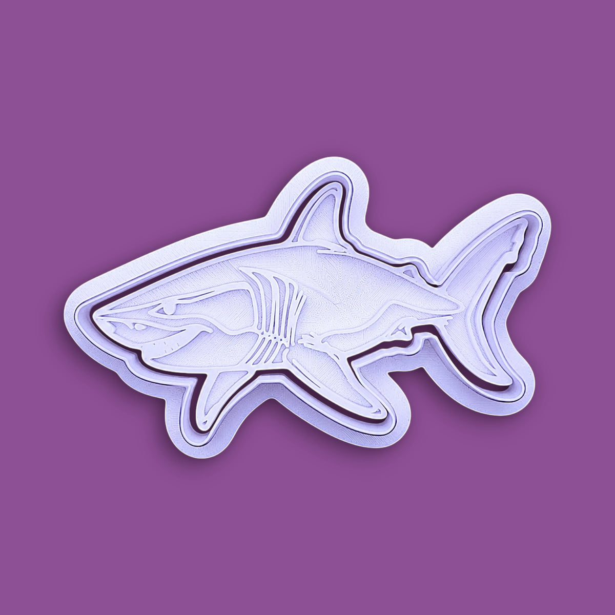 A white plastic shark-shaped cookie cutter or mold, shown from a side profile against a solid purple background.