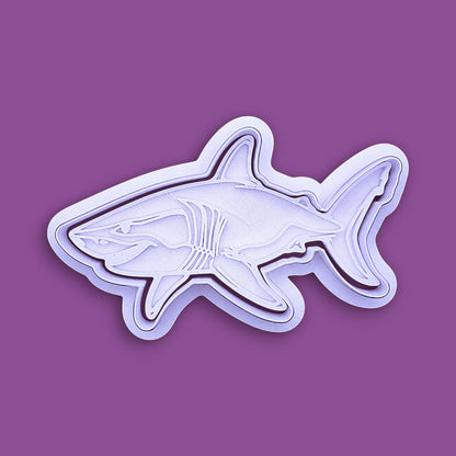 A white plastic shark-shaped cookie cutter or mold, shown from a side profile against a solid purple background.