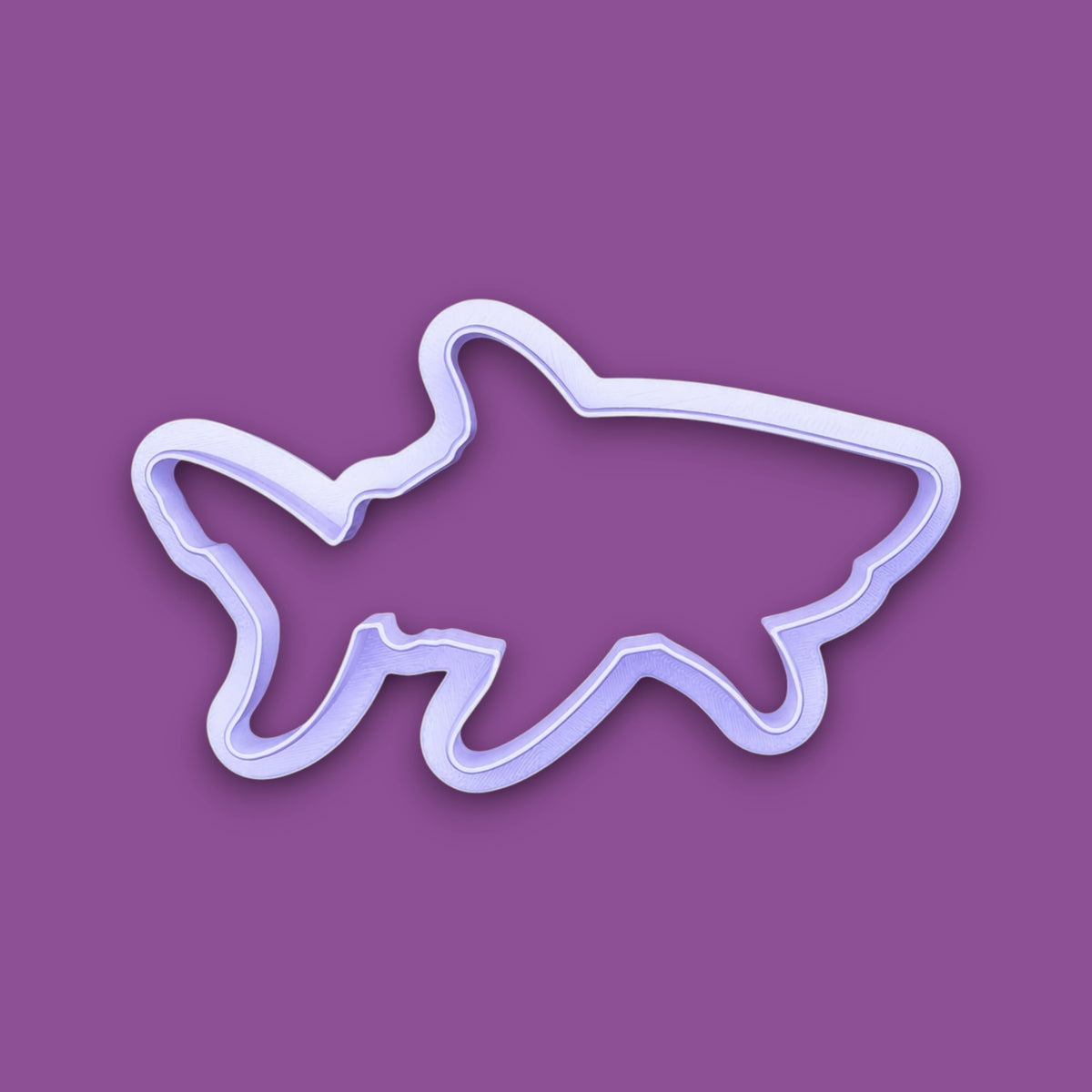 A plastic cookie cutter in the shape of a shark, shown on a solid purple background.