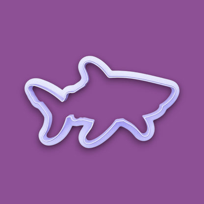 A plastic cookie cutter in the shape of a shark, shown on a solid purple background.