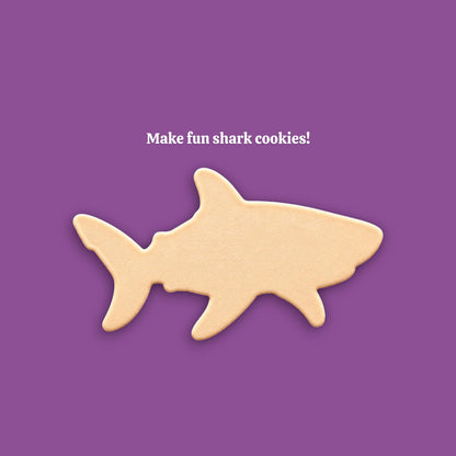 A shark-shaped cookie centered on a solid purple background, with the white text 'Make fun shark cookies!' above it.