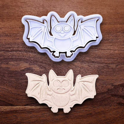 Bat cookie cutter with matching stamp and dough cutout with bat design pressed by cutter and stamp set, showing detailed lines—great for easy Halloween cookie decorating without icing.