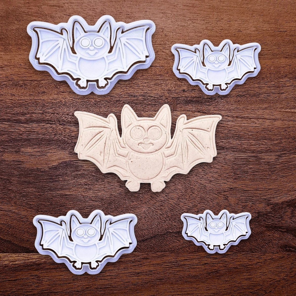 Bat cookie cutters with matching stamps and dough cutout with bat design pressed by cutter and stamp set, showing detailed lines—great for easy Halloween cookie decorating without icing.