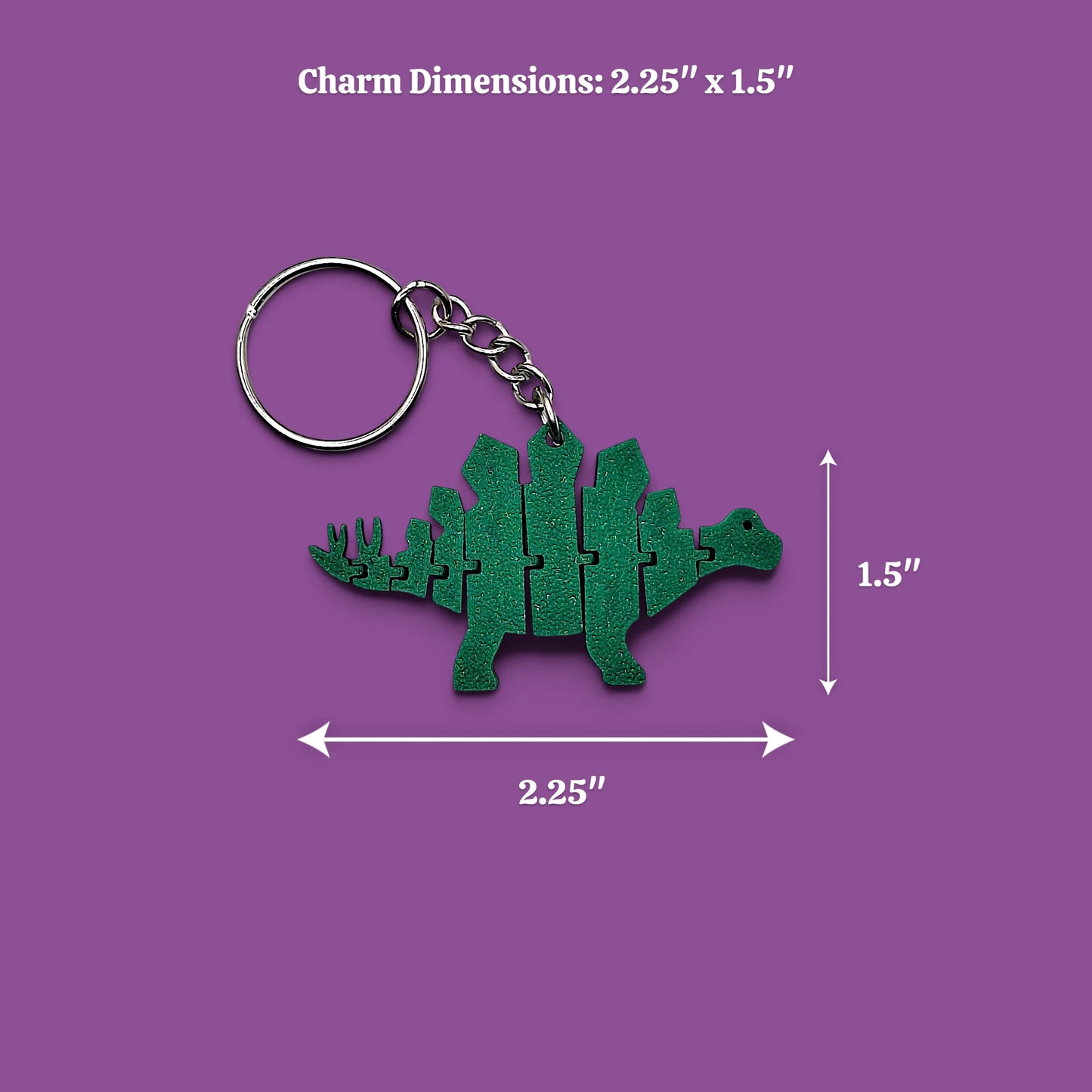 A green dinosaur-shaped keychain charm with a metal split ring and chain, shown on a purple background with dimension arrows and text reading Charm Dimensions: 2.25" x 1.5"