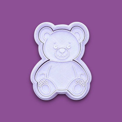 A plastic teddy bear-shaped cookie cutter and stamp, shown from a top-down view on a solid gray background.