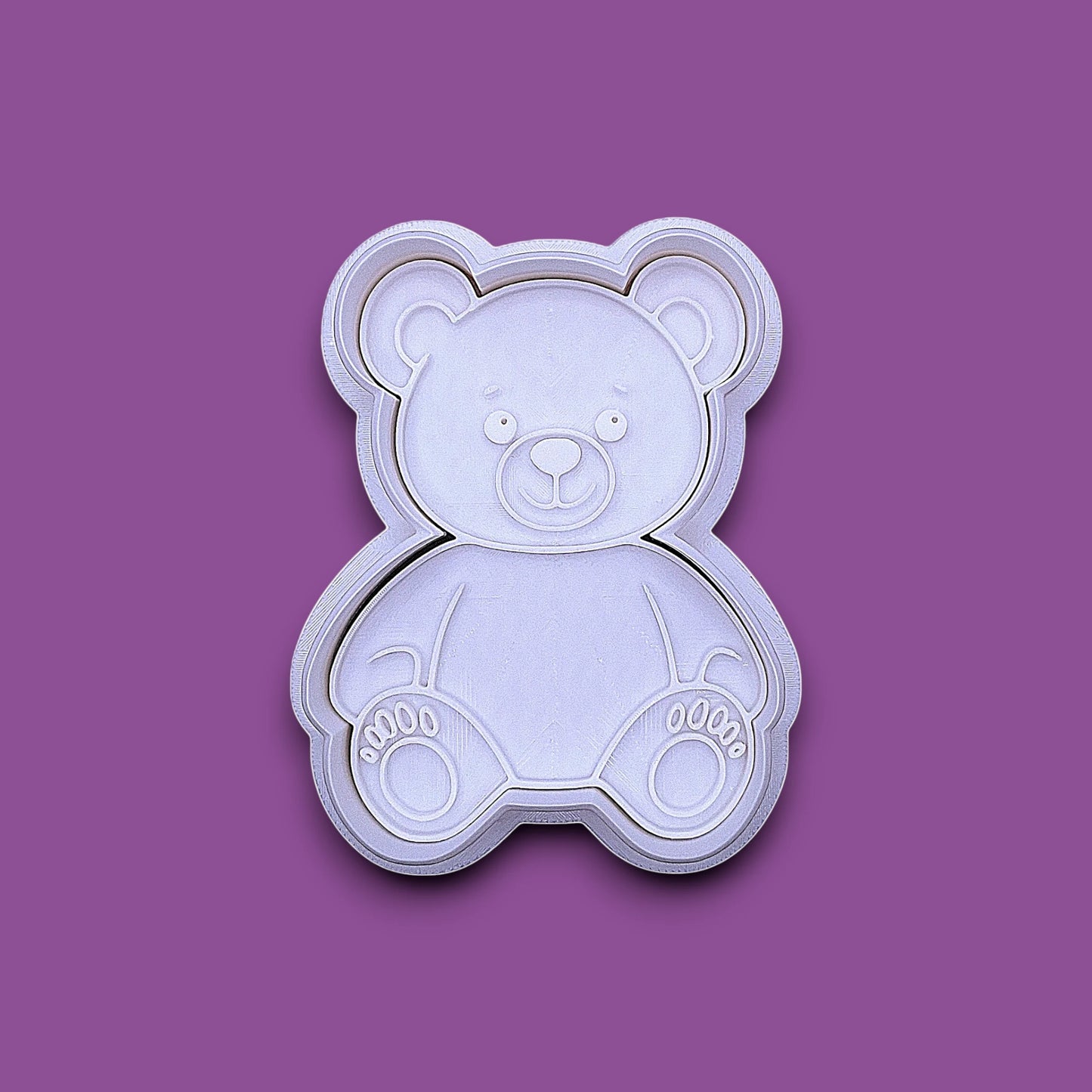 A plastic teddy bear-shaped cookie cutter and stamp, shown from a top-down view on a solid gray background.