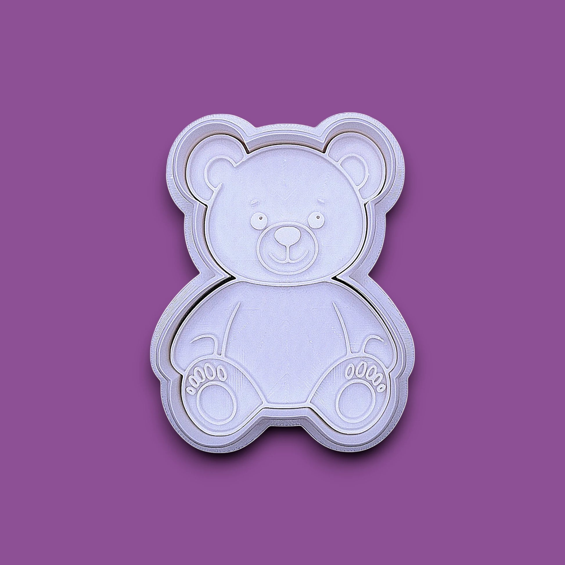 A plastic teddy bear-shaped cookie cutter and stamp, shown from a top-down view on a solid gray background.