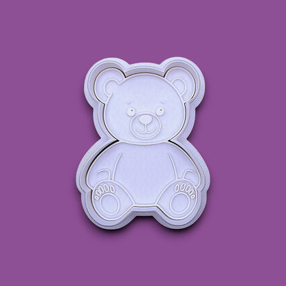 A plastic teddy bear-shaped cookie cutter and stamp, shown from a top-down view on a solid gray background.