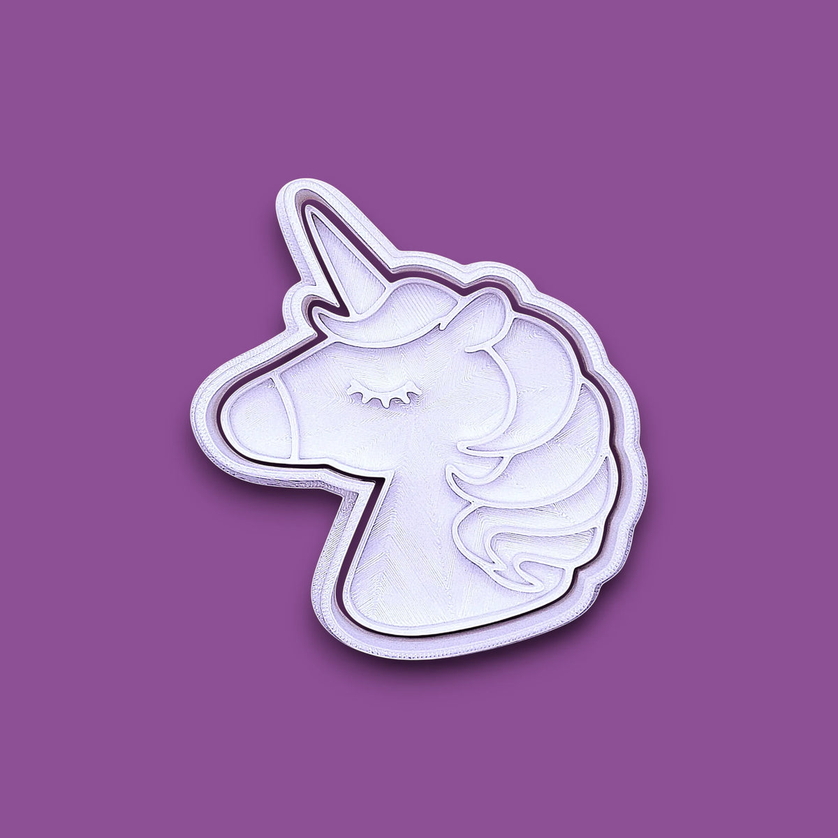 A white unicorn head cookie cutter with a purple border, shown on a solid purple background.