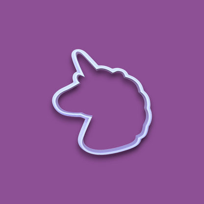 A white plastic cookie cutter shaped like a unicorn head, shown on a solid purple background.